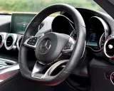 Interior de un coche deportivo Mercedes-AMG. Volante de cuero negro con controles, logo de Mercedes y detalles AMG.