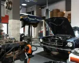 Plano de taller mecánico con dos coches clásicos, uno azul en elevador y otro negro con capó abierto.